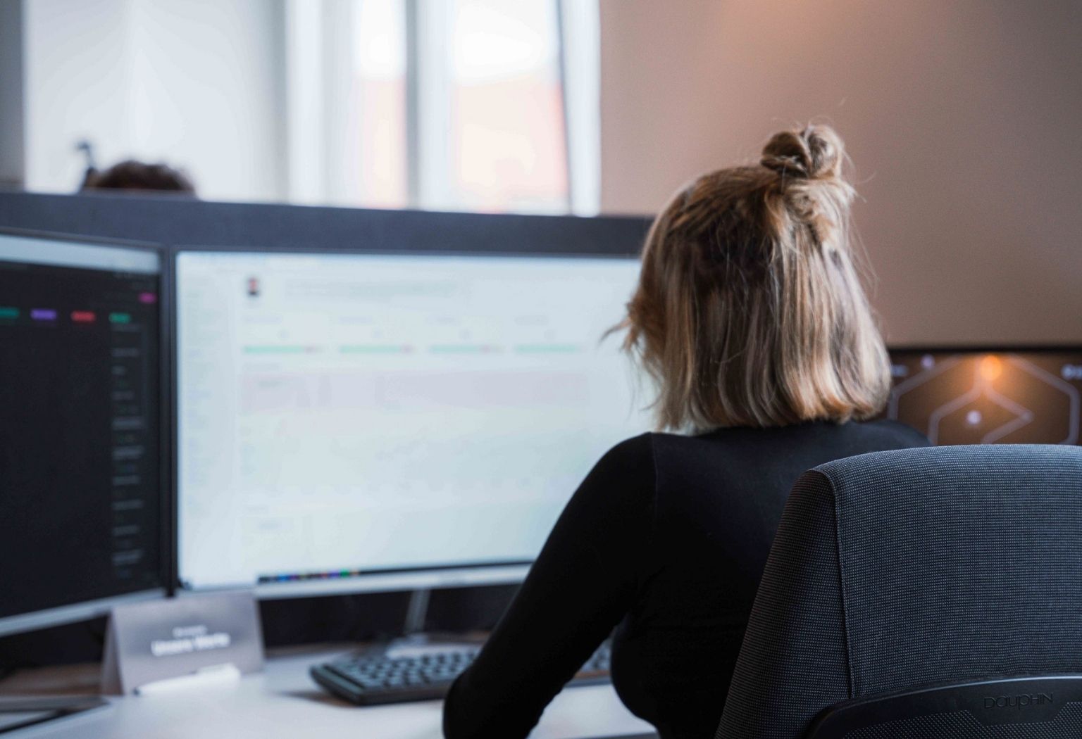 Eine Frau sitzt an einem Schreibtisch vor zwei Computerbildschirmen und arbeitet konzentriert.